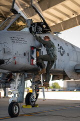 A man in a green uniform is climbing up the side of a fighter jet