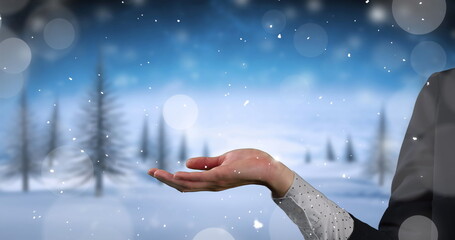 Image of snow falling over hands of caucasian woman and winter landscape
