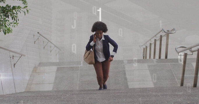 Image of numbers over african american businesswoman talking on smartphone while climbing stairs - Powered by Adobe