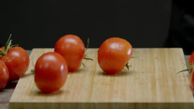 wooden cutting board with washed tomatoes rolling on it against an abstract background is seen in the camera's view. Close up. Slow motion.