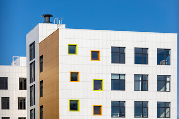 Corner fragment of building with windows of different sizes and ventilated facade made of white composite panels. Modern technology of building facades design