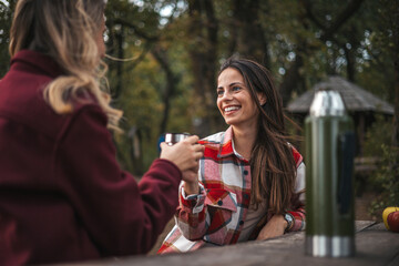 Camp coffee is the best coffee.  Female hikers cheering up with camping cups, camping in forest,...