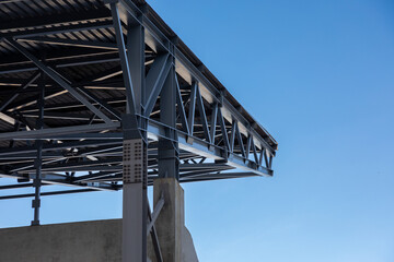 Fragment of a canopy. Metal beams on a concrete base support a metal roof against a blue sky - obrazy, fototapety, plakaty