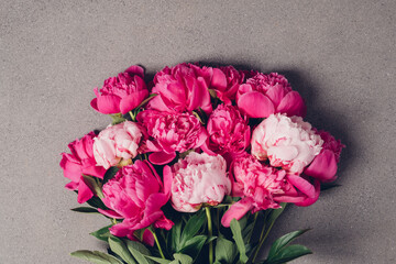 Beautiful bunch of fresh fluffy pink peony flowers in full bloom on dark grey background, top view, flat lay style.