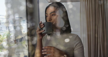 Image of light spots over biracial woman holding mug and drinking