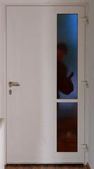 Ein Einbrecher steht in der Dunkelheit mit einer Pistole vor einer Eingangstüre und schaut durch...