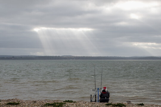 Fisherman  wearing a Christmas hat on the beach at Lee On The Solent  with The Isle of Wight Hampshire England in the background