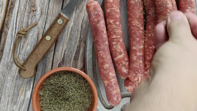 main humaine versant des herbes, en gros plan, sur des saucisses crues