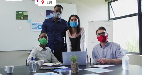 Image of social media icons over portrait of diverse colleagues wearing face masks at office