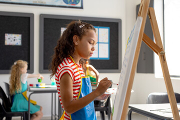In school art class, biracial girl painting, two friends sitting behind
