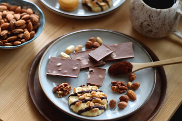 Cup of tea or coffee, cookies, macaroons, chocolate, various nuts and cocoa powder on wooden table. Selective focus.