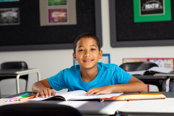 In school, young biracial male student sitting at a desk in a classroom, smiling