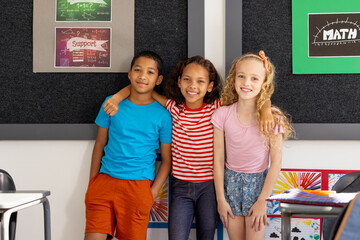 In school, three young students posing together in the classroom, two biracial and one Caucasian