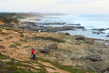 nice senior woman riding her electric mountain bike at the rocky and sandy coastline of the...