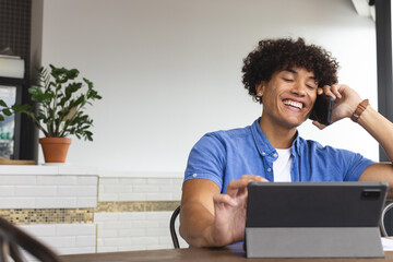 A young biracial man wearing a blue shirt is talking on the phone in a modern business office - 785550011