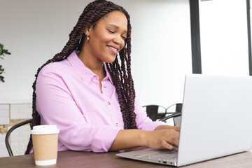 Young biracial woman wearing pink shirt working on laptop