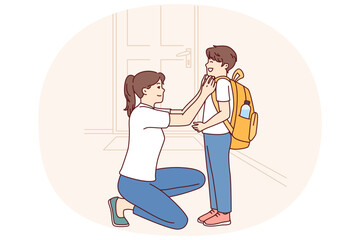 Single mother prepares young son of student in elementary school as trip to lessons and helps to put on briefcase kneeling down. Caring mother dresses teen boy for first day of school - 785550040