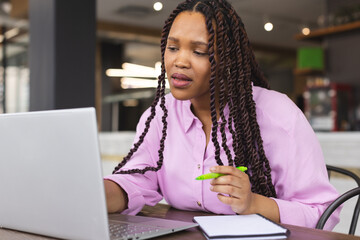 Young biracial woman with long braided hair working on laptop in a modern business office - 785550221