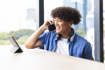 A young biracial man with curly hair is talking on the phone in a modern business office - 785550226