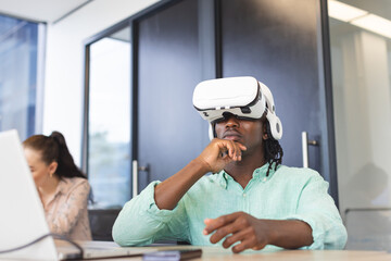 African American man wearing virtual reality headset, thinking, in a modern business office - 785550695