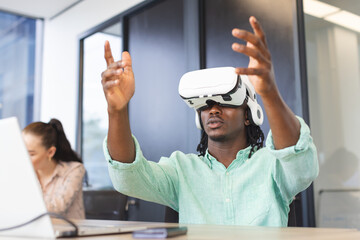 African American man wearing virtual reality headset, gesturing in a modern business office - 785550697
