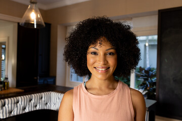 Biracial young woman standing in kitchen, smiling at camera at home
