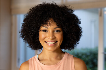 Biracial young woman with curly black hair smiling at camera at home