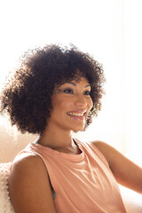 Biracial young woman sitting at home, looking away, smiling gently