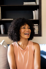 Biracial young woman laughing, sitting on couch at home