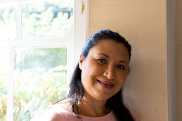 Mature biracial woman standing by window, looking calm at home