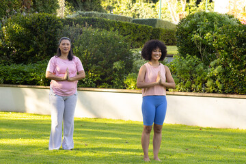 Mature biracial mother and adult daughter practicing yoga in garden at home