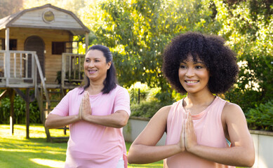 Mature biracial woman and young biracial woman doing yoga in garden at home