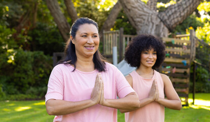 Mature biracial woman and young biracial woman practicing yoga in garden at home