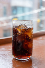 A can-shaped glass of Cola on the table with bokeh background