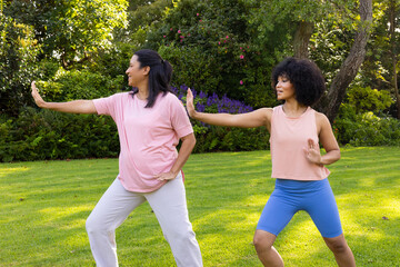 Biracial mother and daughter practicing yoga in garden at home