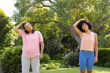 Mature biracial woman and young biracial woman stretching in park at home