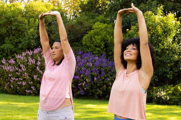 Mature biracial woman and young biracial woman are stretching in garden at home