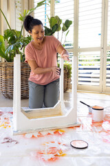 Mature biracial woman painting furniture at home in an upcycling project, wearing casual clothes