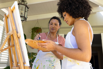 Mother and Daughter, mature biracial woman and young biracial woman painting together at home - Powered by Adobe