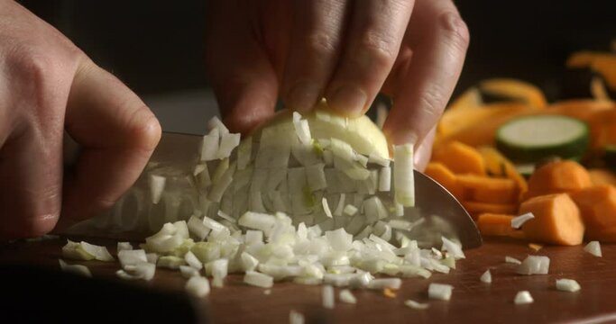 Super slow motion macro of fresh bio organic white onion is being cut in slices by chef with sharp blade knife on wooden cut board while preparing vegetarian salad dish in restaurant kitchen.