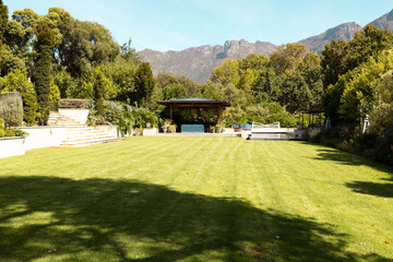 Lush green lawn stretches towards gazebo with mountains in background at home - 785553021