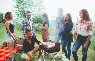 Group of friends eat in a farmhouse in the countryside. Moments of happiness and positive vibrations in contact with nature. Young people making barbeque outdoor. - obrazy, fototapety, plakaty