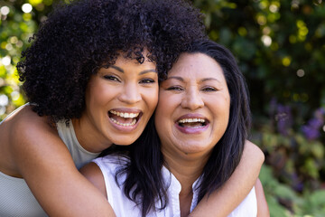 Biracial mother and adult daughter are laughing together outdoors at home in the garden - obrazy, fototapety, plakaty