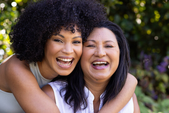Biracial mother and adult daughter are laughing together outdoors at home in the garden