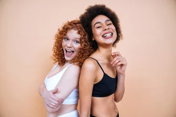 Poster Beauty image of two young smiling and happy women with different body posing in studio for a body positive photoshooting. Mixed female models in lingerie on colored backgrounds.  © oneinchpunch