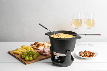 Fondue pot with tasty melted cheese, forks, wine and different snacks on white wooden table