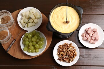 Fondue pot with tasty melted cheese, forks, wine and different snacks on wooden table, flat lay