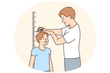 Smiling father measure son height near wall