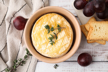 Tasty baked camembert in bowl, grapes, croutons and thyme on wooden table, flat lay