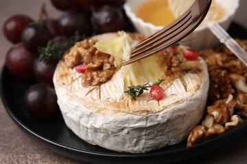 Taking tasty baked camembert with fork from plate at brown table, closeup